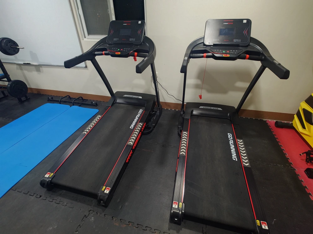 フィリピンのバギオにあるMONOL Sparta Campusの校内ジムに設置された2台のトレッドミル。黒と赤のランニングマシンが横並びに配置され、左側には青いエクササイズマットが敷かれている