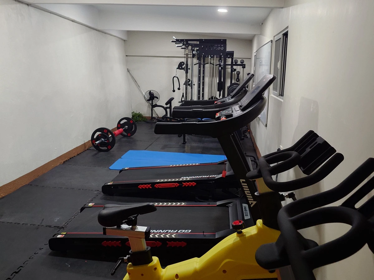 フィリピンのバギオにあるMONOL Sparta Campusの校内ジム全景。細長い室内にトレッドミルと黄色いスピンバイクが並び、奥には筋力トレーニング用のマルチジム、左側にはバーベルや青いエクササイズマットが配置されている
